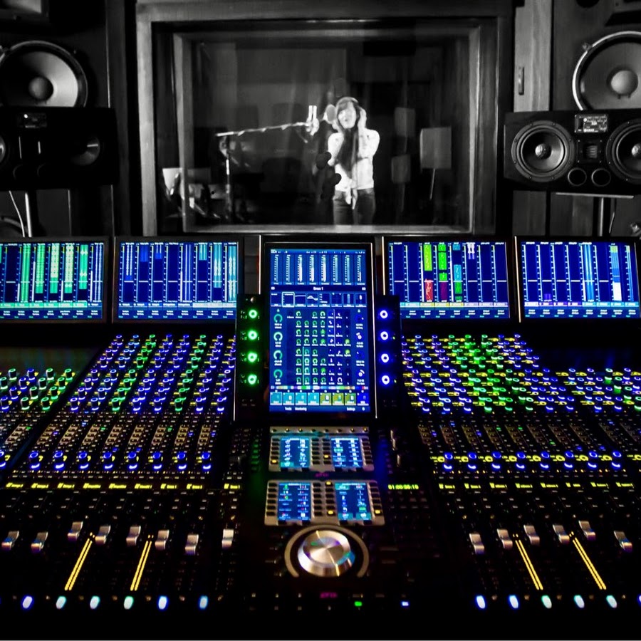 A recording studio's mixing console is in focus, with a vocalist performing in the background.